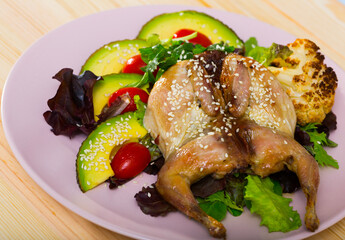 Photography of plate with quail-tobacco with sesame which served with salad of avocado and greenery in restaurante.