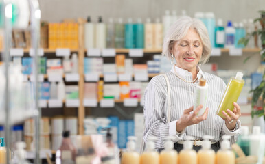 Elderly female shopper in summer clothes chooses medicated shampoo at a pharmacy