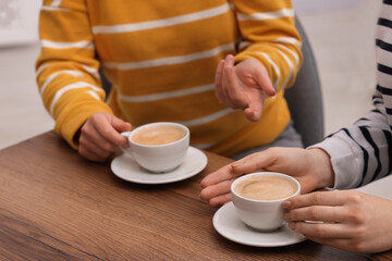 Coffee break. Women with cups of hot drinks at wooden table indoors, closeup