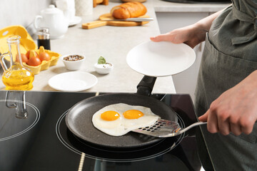 Woman taking fried eggs from frying pan in kitchen, closeup