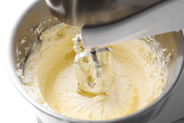 Mixing whipped cream in bowl with stand mixer on white table, closeup