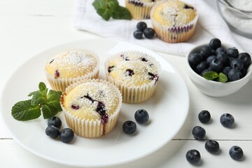 Delicious muffins with blueberries, powdered sugar and mint on white wooden table, closeup