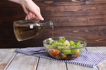 Woman pouring oil onto tasty salad at color wooden table, closeup