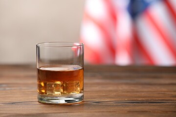 Glass of whiskey on wooden table against American flag. Space for text