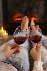 Couple with glasses of wine near fireplace on floor at home, closeup