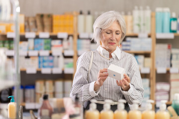 Elderly woman buyer chooses box of pills in pharmacy