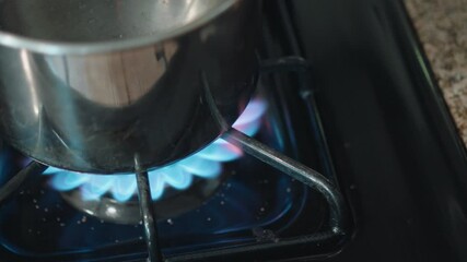 Lit gas stove burner with a pot on it, showing the blue flame and active cooking