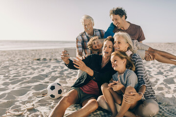 Multigenerational family taking a selfie with a smartphone on a sandy beach on their holiday vacation