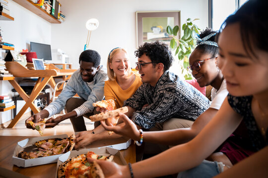 Group of diverse young friends eating pizza in a shared apartment