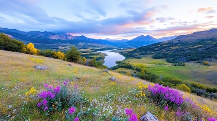 Fototapeta premium Scenic mountain valley landscape with a winding river, green hills, and purple wildflowers in the foreground under a sunset sky.