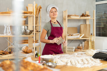 Female baker cutting raw dough with knife on kitchen table in bakery