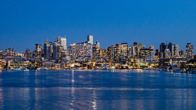 An expansive view of Seattle's downtown skyline captured during the blue hour, with shimmering city lights reflecting over the calm waters of Lake Union. This image highlights the modern architecture 