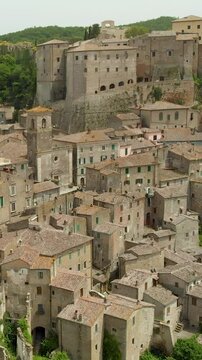 Aerial summer afternoon view of Sorano. Rooftops of an ancient medieval hill town hanging from a tuff stone over the Lente River. Etruscan heritage. Province Grosseto, Tuscany, Italy. Vertical footage