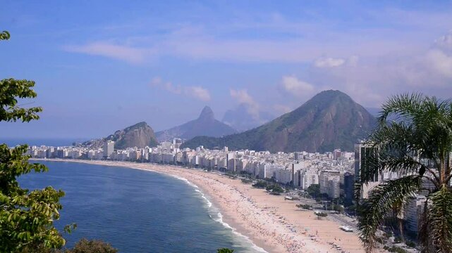 Copacabana Beach in Rio de Janeiro, with sand and sea in the foreground and mountains and blue sky in the background. Aerial view.
