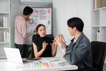 Creativity and Collaboration. A graphic design team brainstorming around a laptop, discussing color palettes and design concepts.