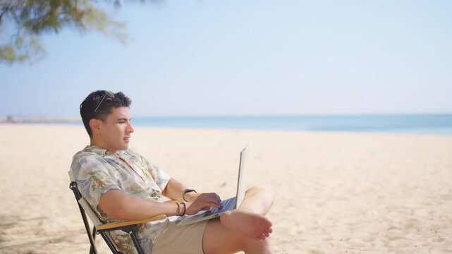 Asian man remote working corporate business on laptop computer during travel the beach on summer holiday vacation. Workation, work from anywhere with wireless technology and digital gadget device.