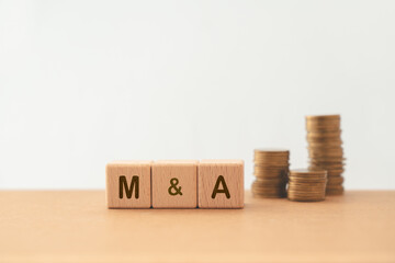 M and A, Mergers and Acquisitions, text on wooden cube blocks with blurred stack of coins  including copy space
