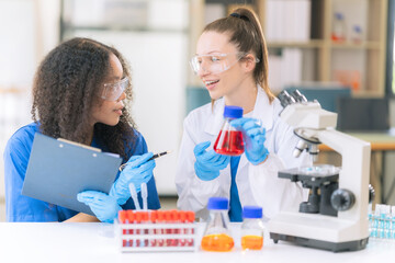 Two female scientists examine liquids in test tubes in a modern laboratory, handling chemicals and...