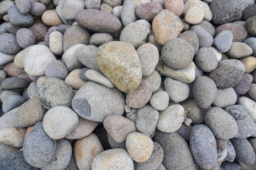 A natural pile of smooth river stones stacked together, shaped by flowing water and time, creating a serene and earthy scene by the riverbank.
