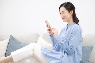 リビングのソファーに座って、スマホを見る女性の横顔 ネットショッピングや検索