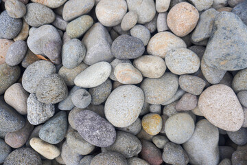 A natural pile of smooth river stones stacked together, shaped by flowing water and time, creating a serene and earthy scene by the riverbank.