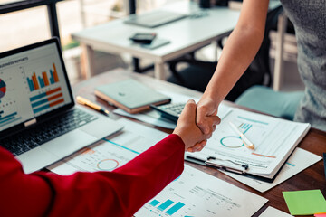 Collaboration agreement of entrepreneurs shaking hands in modern office with calculator and financial documents on wooden table symbolizing a successful business agreement.