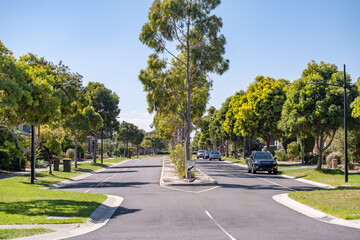 A suburban intersection with a straight asphalt road framed by mature trees and manicured lawns on...