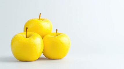Three bright yellow apples, slightly wet, stacked on a plain background