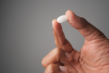 Person holding a white pill between fingers in a neutral setting