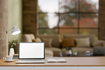 The white screen laptop on wooden table in the earth tone living room or a lounge with brick wall.