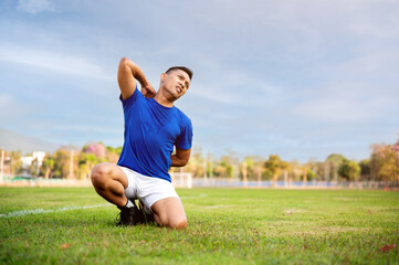 Asian man in blue t shirt is kneeling on grass and touching or massaging his back.Pain or injury.