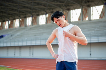 Asian man standing with one hand on waist and other hand fanning himself with white tank top.