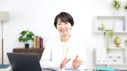 カメラ目線で会話する白衣のミドル女性