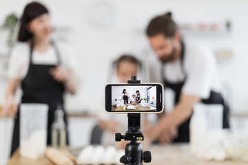 Caucasian family blogging their culinary activity, including dancing and dough kneading, in modern...