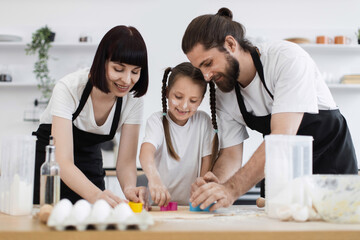 Obraz premium Caucasian family, including a young daughter, joyfully baking cookies together in a modern kitchen. They use molds to cut dough and share a fun, bonding experience full of smiles and creativity.