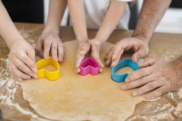 Family preparing cookies with hands using heart-shaped molds on rolled dough, showcasing teamwork.