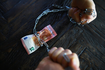 Hands Bound by Chains with Euro Currency Note on Dark Wooden Surface Depicting Financial Constraints