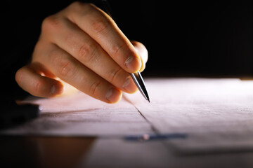 Close-Up of Hand Writing with Pen on Document in Dark Room