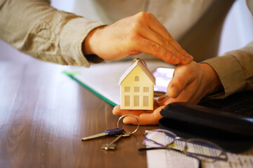Protecting Your Home Investment - Hands Shielding House Model with Keys and Documents