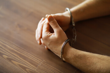 Close-Up of Hands in Handcuffs on Wooden Table - Arrest, Law, Crime, Justice Concept