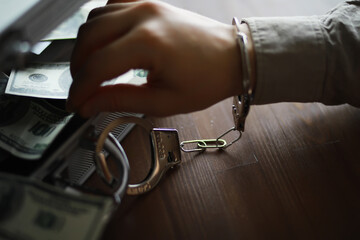 Handcuffed Hand Reaching for Money in Briefcase Indicating Financial Crime and Corruption