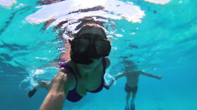 woman snorkeling in the sea with a face mask and snorkel, in a pink swimsuit, with a massive sports watch, man in the background