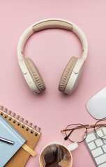 Wireless headphones, coffee, keyboard, eyeglasses, and notebook on pink table
