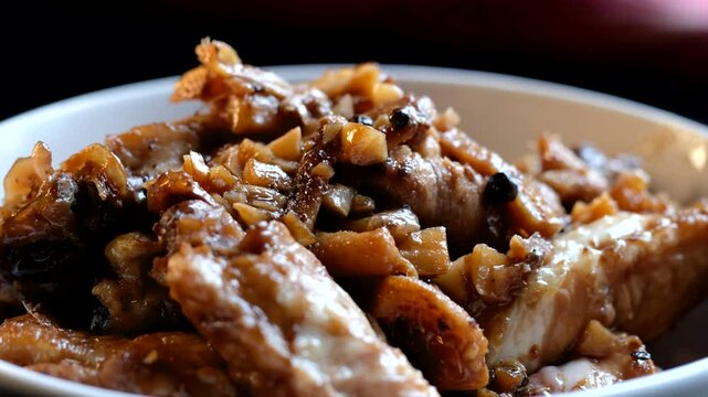 A white bowl of chicken adobo. Chunks of cooked meat and a dark sauce appear moist and savory.