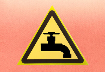 Warning sign "water tap" in the form of a yellow triangle on a light background close-up