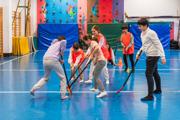 Group of children wearing bibs, enthusiastically playing floorball together in a vibrant school...