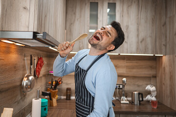 Man holds a spatula in his apron and sings in the kitchen