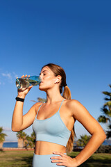 Sporty woman drinking water from bottle after training outdoors in park