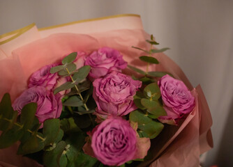 A bouquet of purple flowers with green leaves. The flowers are arranged in a pink wrapping