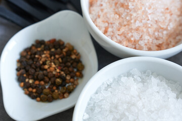 Various kinds of salt and peppercorns in white bowls on wooden background